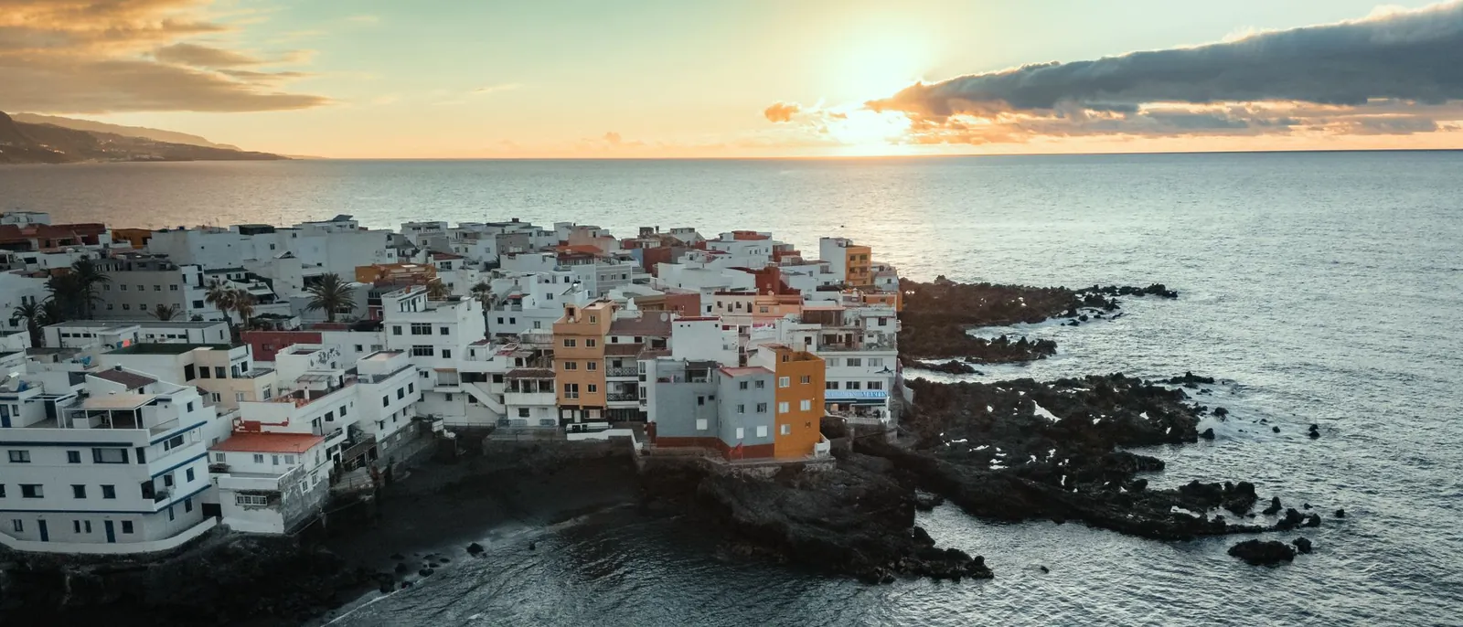 Casas blancas junto a una costa de roca volcánica oscura en Tenerife, al atardecer