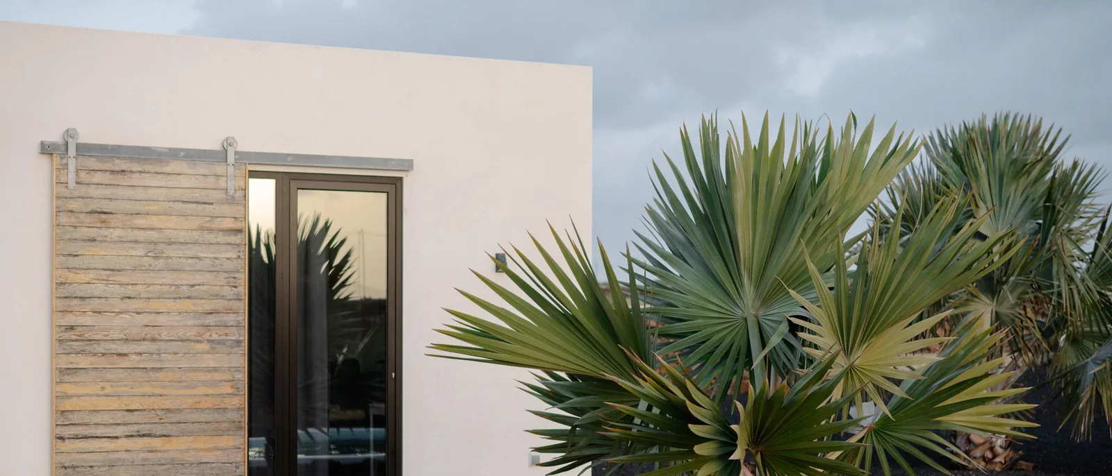 Casa de muros blancos con puerta corredera de madera y palmeras de abanico