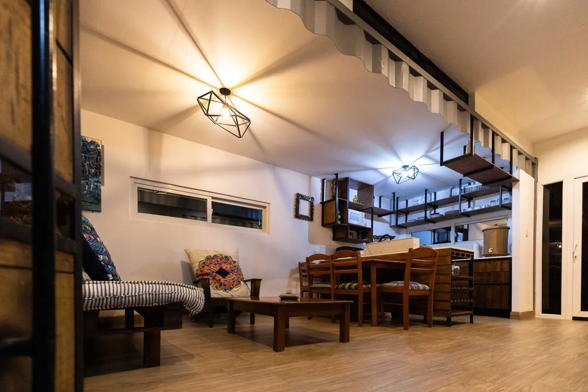 Salón y cocina abiertos de una vivienda modular con techo de chapa ondulada y estantes de madera