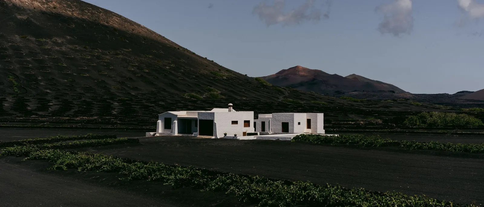 Casa blanca de líneas sencillas en un paisaje volcánico con viñas bajo un cielo azul