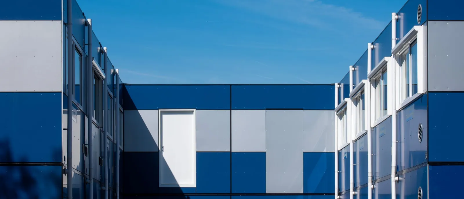 Edificio de viviendas modulares con paneles azules y grises y ventanas bajo un cielo despejado