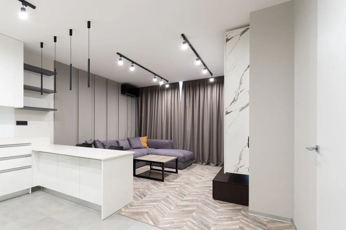 Salón con cocina abierta, sofá y suelo de dos materiales en una vivienda moderna
