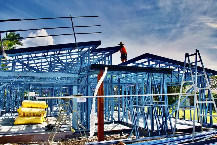 Estructura de acero ligero de una vivienda en construcción, con perfiles azules y cubierta a medio montar bajo un cielo con nubes