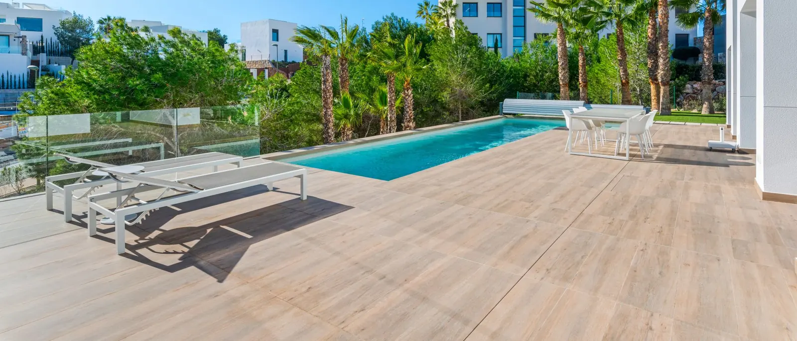 Terraza soleada de una vivienda moderna de paredes blancas, con piscina, tumbonas y palmeras bajo un cielo despejado