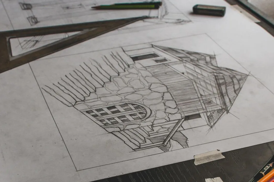Dibujo a lápiz del proyecto de una casa sobre una mesa de dibujo, con escuadra, lápices y cinta
